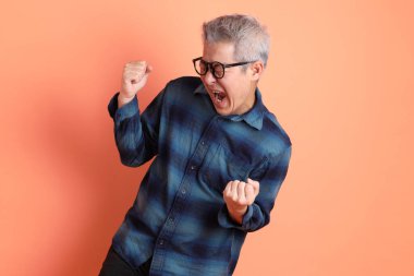 Yeşil ekose elbiseli Asyalı son sınıf öğrencisi gözlüklü, evet jestli, heyecanlı, turuncu arka planda izole edilmiş kutlamayı kutluyor. Turist, akıllı gündelik.