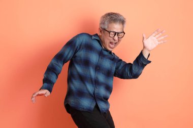 Yeşil ekose giysili Asyalı son sınıf öğrencisi gözlüklü, turuncu arka planda izole edilmiş dans jestli. Turist, akıllı gündelik.