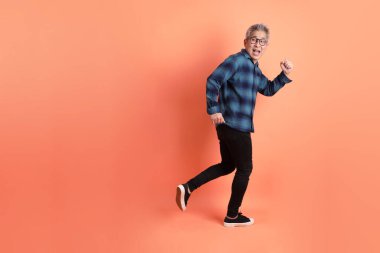 Yeşil ekose giysili Asyalı son sınıf öğrencisi gözlüklü turuncu arka planda izole edilmiş yürüyüş jesti yapıyor. Turist, akıllı gündelik.