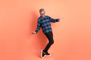 Yeşil ekose giysili Asyalı son sınıf öğrencisi gözlüklü, turuncu arka planda izole edilmiş dans jestli. Turist, akıllı gündelik.