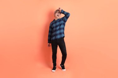 Yeşil ekose giysili Asyalı son sınıf öğrencisi gözlüklü ve turuncu arka planda izole edilmiş stres jesti takıyor. Turist, akıllı gündelik.