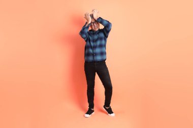 Yeşil ekose giysili Asyalı son sınıf öğrencisi gözlüklü ve turuncu arka planda izole edilmiş stres jesti takıyor. Turist, akıllı gündelik.