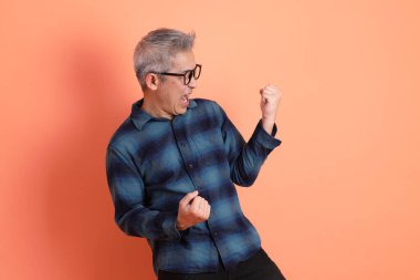 Yeşil ekose elbiseli Asyalı son sınıf öğrencisi gözlüklü, evet jestli, heyecanlı, turuncu arka planda izole edilmiş kutlamayı kutluyor. Turist, akıllı gündelik.