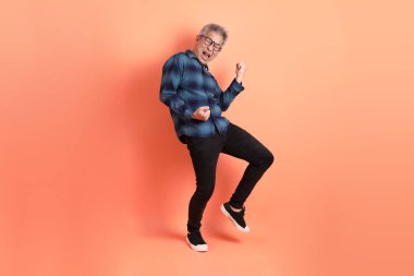 Yeşil ekose elbiseli Asyalı son sınıf öğrencisi gözlüklü, evet jestli, heyecanlı, turuncu arka planda izole edilmiş kutlamayı kutluyor. Turist, akıllı gündelik.