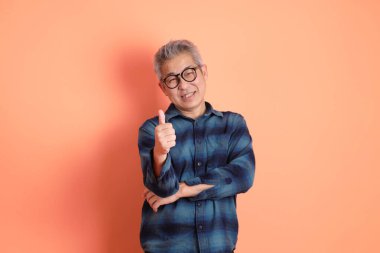 Yeşil ekose giysili Asyalı son sınıf öğrencisi. Gözlük takıyor. Başparmak işareti yapıyor. Turist, akıllı gündelik.