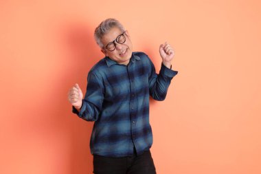 Yeşil ekose elbiseli Asyalı son sınıf öğrencisi gözlüklü, evet jestli, heyecanlı, turuncu arka planda izole edilmiş kutlamayı kutluyor. Turist, akıllı gündelik.