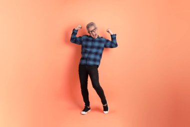 Yeşil ekose elbiseli Asyalı son sınıf öğrencisi gözlüklü, evet jestli, heyecanlı, turuncu arka planda izole edilmiş kutlamayı kutluyor. Turist, akıllı gündelik.