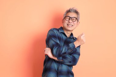 Yeşil ekose giysili Asyalı son sınıf öğrencisi gözlüklü, ayakta duran ve turuncu arka planda sırıtan. Turist, akıllı gündelik.