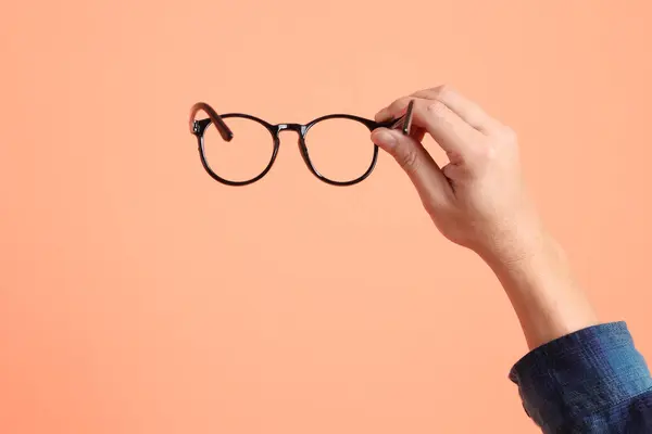 Yeşil ekose elbiseli Asyalı son sınıf öğrencisi. Turuncu arka planda gözlük tutan el hareketleriyle. Turist, akıllı gündelik.