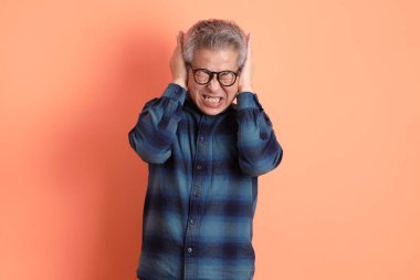 Yeşil ekose giysili Asyalı son sınıf öğrencisi. Gözlük takıyor. Kulağı kapalı, turuncu arka planda. Turist, akıllı gündelik.