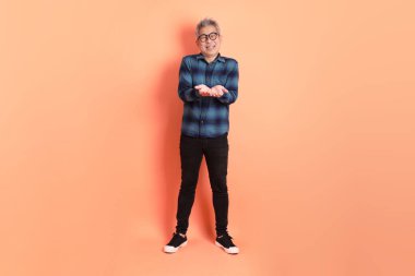 Yeşil ekose giysili Asyalı son sınıf öğrencisi. Gözlük takıyor. Turuncu arka planda izole edilip alınma hareketi yapıyor. Turist, akıllı gündelik.