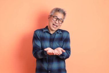 Yeşil ekose giysili Asyalı son sınıf öğrencisi. Gözlük takıyor. Turuncu arka planda izole edilip alınma hareketi yapıyor. Turist, akıllı gündelik.