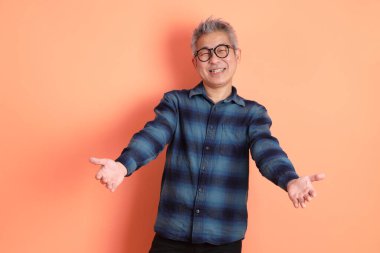 Yeşil ekose giysili Asyalı son sınıf öğrencisi. Gözlük takıyor. Turuncu arka planda izole edilip alınma hareketi yapıyor. Turist, akıllı gündelik.