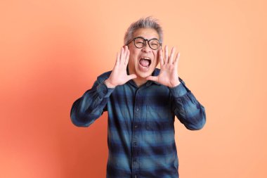 Yeşil ekose giysili Asyalı son sınıf öğrencisi. Gözlük takıyor. Bağırıyor, elinde turuncu arka planda megafon tutuyor. Turist, akıllı gündelik.