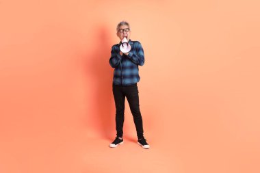 Yeşil ekose giysili Asyalı son sınıf öğrencisi. Gözlük takıyor. Bağırıyor, elinde turuncu arka planda megafon tutuyor. Turist, akıllı gündelik.