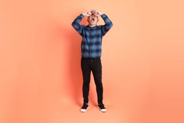 Yeşil ekose elbiseli Asyalı son sınıf öğrencisi. Gözlük takıyor. Hayal kırıklığı jesti, turuncu arka planda yalnız başına ağlıyor. Turist, akıllı gündelik.