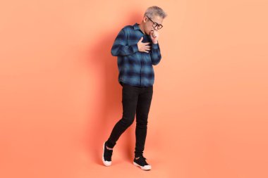 Yeşil ekose giysili Asyalı son sınıf öğrencisi gözlük takıyor ve turuncu arka planda hastalıklı davranışlar sergiliyor. Turist, akıllı gündelik.