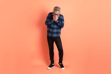 Yeşil ekose giysili Asyalı son sınıf öğrencisi gözlük takıyor ve turuncu arka planda hastalıklı davranışlar sergiliyor. Turist, akıllı gündelik.