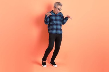 Yeşil ekose giysili Asyalı son sınıf öğrencisi gözlük takıyor ve turuncu arka planda hastalıklı davranışlar sergiliyor. Turist, akıllı gündelik.