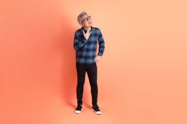 Yeşil ekose giysili Asyalı son sınıf öğrencisi gözlük takıyor ve turuncu arka planda hastalıklı davranışlar sergiliyor. Turist, akıllı gündelik.