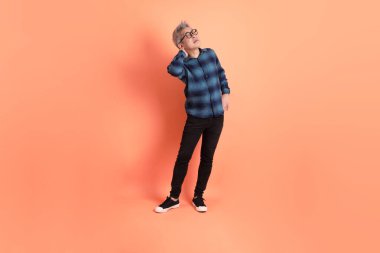 Yeşil ekose giysili Asyalı son sınıf öğrencisi. Gözlük takıyor. Sırt ağrısı jesti turuncu arka planda. Turist, akıllı gündelik.