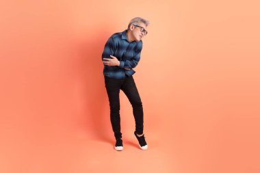 Yeşil ekose giysili Asyalı son sınıf öğrencisi. Gözlük takıyor. Sırt ağrısı jesti turuncu arka planda. Turist, akıllı gündelik.