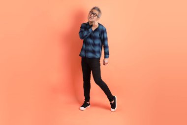 Yeşil ekose giysili Asyalı son sınıf öğrencisi. Gözlük takıyor. Sırt ağrısı jesti turuncu arka planda. Turist, akıllı gündelik.