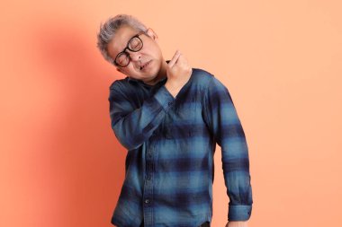 Yeşil ekose giysili Asyalı son sınıf öğrencisi. Gözlük takıyor. Sırt ağrısı jesti turuncu arka planda. Turist, akıllı gündelik.