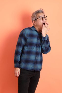 Yeşil ekose elbiseli, gözlüklü, uykulu ya da turuncu arka planda esnemiş Asyalı son sınıf öğrencisi. Turist, akıllı gündelik.