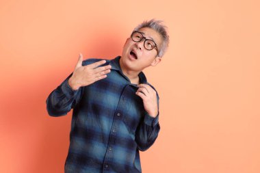 Yeşil ekose elbiseli Asyalı son sınıf öğrencisi gözlük takıyor ve turuncu arka planda kendini izole edilmiş hissediyor. Turist, akıllı gündelik.