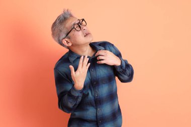 Yeşil ekose elbiseli Asyalı son sınıf öğrencisi gözlük takıyor ve turuncu arka planda kendini izole edilmiş hissediyor. Turist, akıllı gündelik.