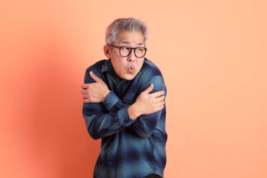 Yeşil ekose giysili Asyalı son sınıf öğrencisi gözlük takıyor ve turuncu arka planda soğuk havası var. Turist, akıllı gündelik.