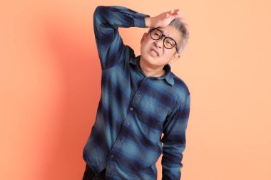 Yeşil ekose elbiseli Asyalı son sınıf öğrencisi gözlük takıyor ve turuncu arka planda kendini izole edilmiş hissediyor. Turist, akıllı gündelik.