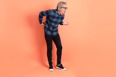 Yeşil ekose giysili Asyalı son sınıf öğrencisi gözlük takıyor ve turuncu arka planda hastalıklı davranışlar sergiliyor. Turist, akıllı gündelik.