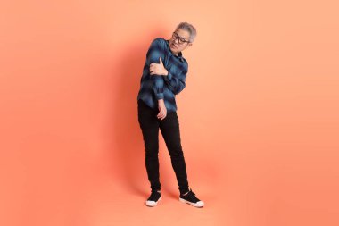 Yeşil ekose giysili Asyalı son sınıf öğrencisi. Gözlük takıyor. Turuncu arka planda izole edilmiş cephanelik işareti var. Turist, akıllı gündelik.