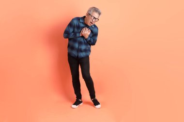 Yeşil ekose elbiseli Asyalı son sınıf öğrencisi gözlük takıyor ve portakal rengi arka planda göğüs ağrısı var. Turist, akıllı gündelik.