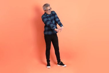 Yeşil ekose giysili Asyalı son sınıf öğrencisi gözlüklü, turuncu arka planda soyutlanmış bir jest yapıyor. Turist, akıllı gündelik.