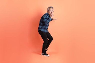 Yeşil ekose elbiseli Asyalı son sınıf öğrencisi gözlüklü, ağzı kapalı, turuncu arka planda izole edilmiş sessiz bir jest. Turist, akıllı gündelik.