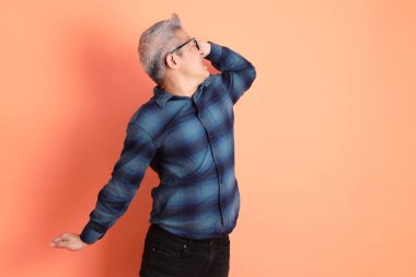 Yeşil ekose giysili Asyalı son sınıf öğrencisi gözlüklü, turuncu arka planda soyutlanmış bir jest yapıyor. Turist, akıllı gündelik.