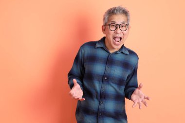 Yeşil ekose giysili Asyalı son sınıf öğrencisi gözlüklü, sürpriz jestli ve turuncu arka planda etkileyici izole edilmiş. Turist, akıllı gündelik.