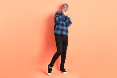 Yeşil ekose giysili Asyalı son sınıf öğrencisi gözlüklü, turuncu arka planda izole edilmiş korku jestli. Turist, akıllı gündelik.