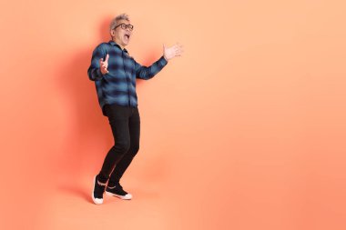 Yeşil ekose giysili Asyalı son sınıf öğrencisi gözlüklü, sürpriz jestli ve turuncu arka planda etkileyici izole edilmiş. Turist, akıllı gündelik.