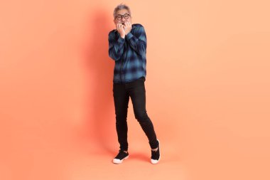 Yeşil ekose giysili Asyalı son sınıf öğrencisi gözlüklü, turuncu arka planda izole edilmiş korku jestli. Turist, akıllı gündelik.