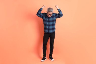 Yeşil ekose elbiseli Asyalı son sınıf öğrencisi gözlük takıyor ve turuncu arka planda öfkeli ve çığlıklar atıyor. Turist, akıllı gündelik.