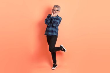 Yeşil ekose giysili Asyalı son sınıf öğrencisi gözlüklü, ayakta duran ve turuncu arka planda sırıtan. Turist, akıllı gündelik.