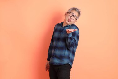 Yeşil ekose giysili Asyalı son sınıf öğrencisi gözlüklü, ayakta duran ve turuncu arka planda sırıtan. Turist, akıllı gündelik.