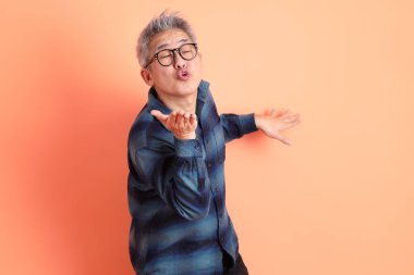 Yeşil ekose giysili Asyalı son sınıf öğrencisi gözlüklü, ayakta duran ve turuncu arka planda sırıtan. Turist, akıllı gündelik.