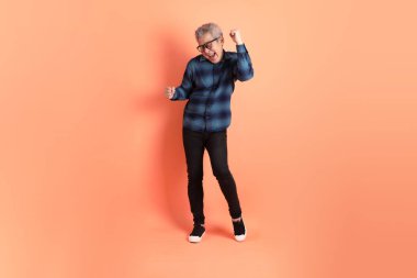 Yeşil ekose giysili Asyalı son sınıf öğrencisi gözlüklü, turuncu arka planda izole edilmiş dans jestli. Turist, akıllı gündelik.