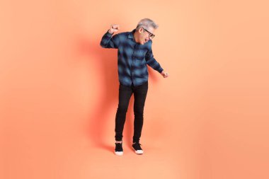 Yeşil ekose giysili Asyalı son sınıf öğrencisi gözlüklü, turuncu arka planda izole edilmiş dans jestli. Turist, akıllı gündelik.