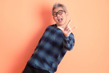 Yeşil ekose elbiseli Asyalı son sınıf öğrencisi. Gözlük takıyor. Kalp şeklinde jestler yapıyor. Turist, akıllı gündelik.